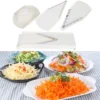 mandoline-de-cuisine-multifonction-set-complet Mandoline de cuisine blanche avec lame en V, protège-main et lames interchangeables, accompagnée de plusieurs assiettes de légumes tranchés en julienne, rondelles et effilochés